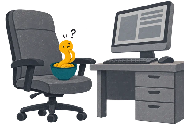Noodle in its bowl on a giant grey office chair, too small to reach a huge grown-up computer